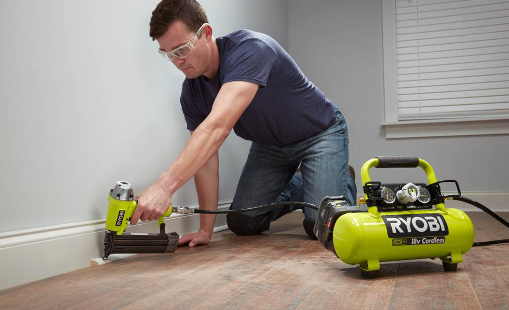 A man using a pneumatic nailer attached to a small air compressor to install moulding.