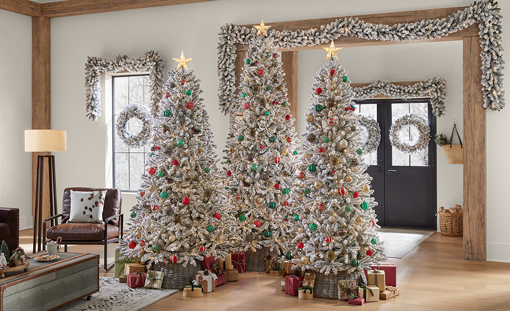 A trio of flocked artificial Christmas trees with red and green decorations.