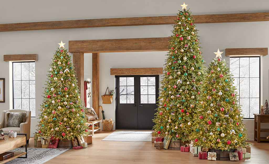 Three decorated artificial balsam fir trees in a holiday living room.