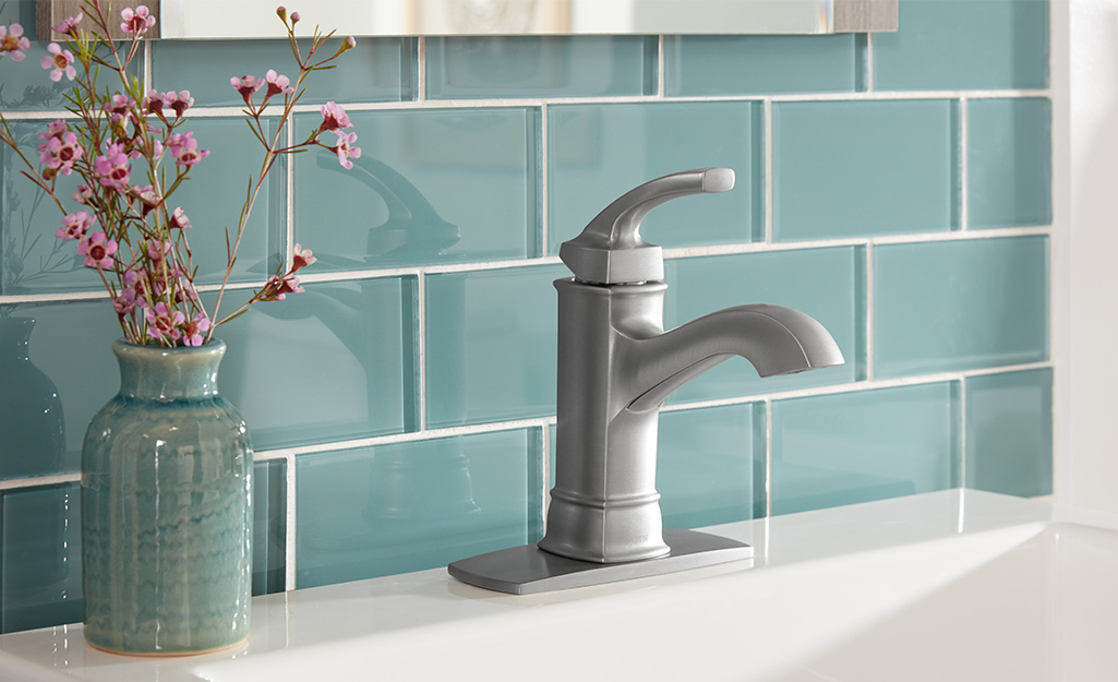 A single-handle bathroom faucet on a white sink, backed by blue tile.