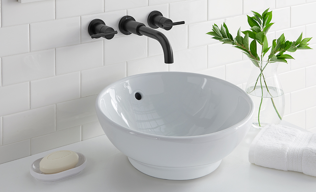 White raised sink installed under a black wall mount faucet.