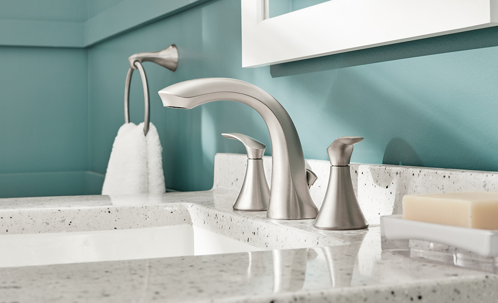 A nickel bathroom faucet with a white sink and black and white countertop.