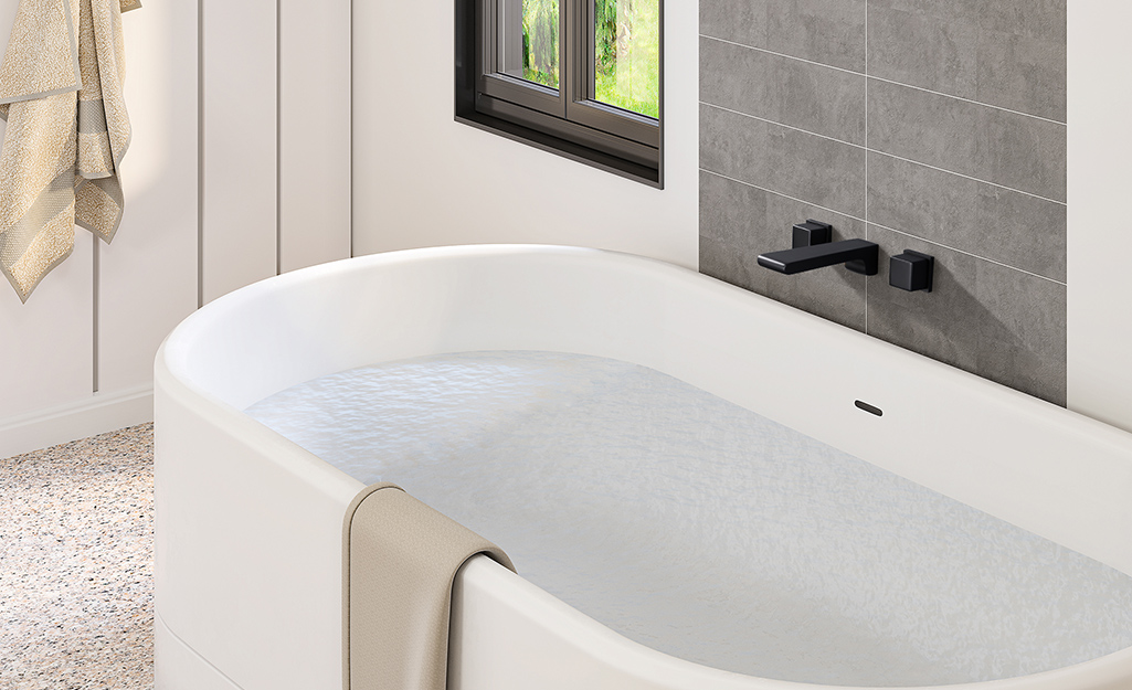 A wall-mounted tub faucet with a dark finish on a white tub.