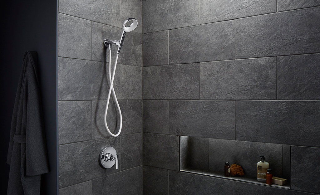 A hand-held shower head in a dark shower.