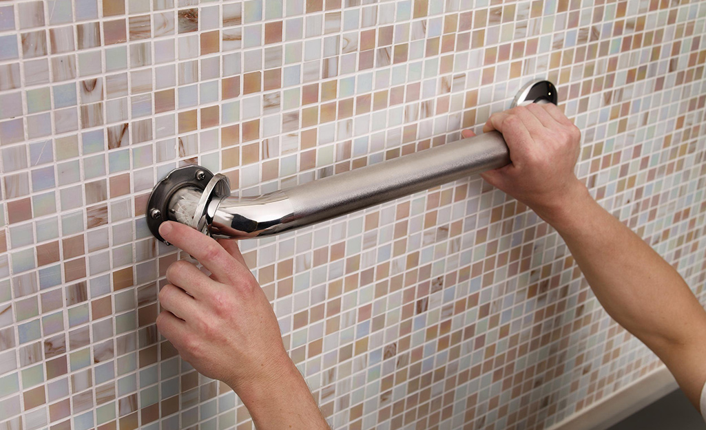 A person installing a grab bar in the bath.