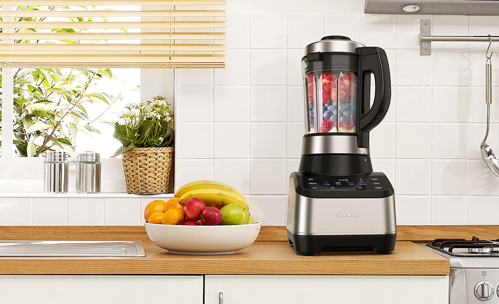 A countertop blender filled with strawberry and blueberry.