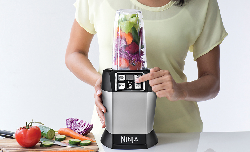 A single serving blender, fruits and vegetables and a travel cup on a counter.
