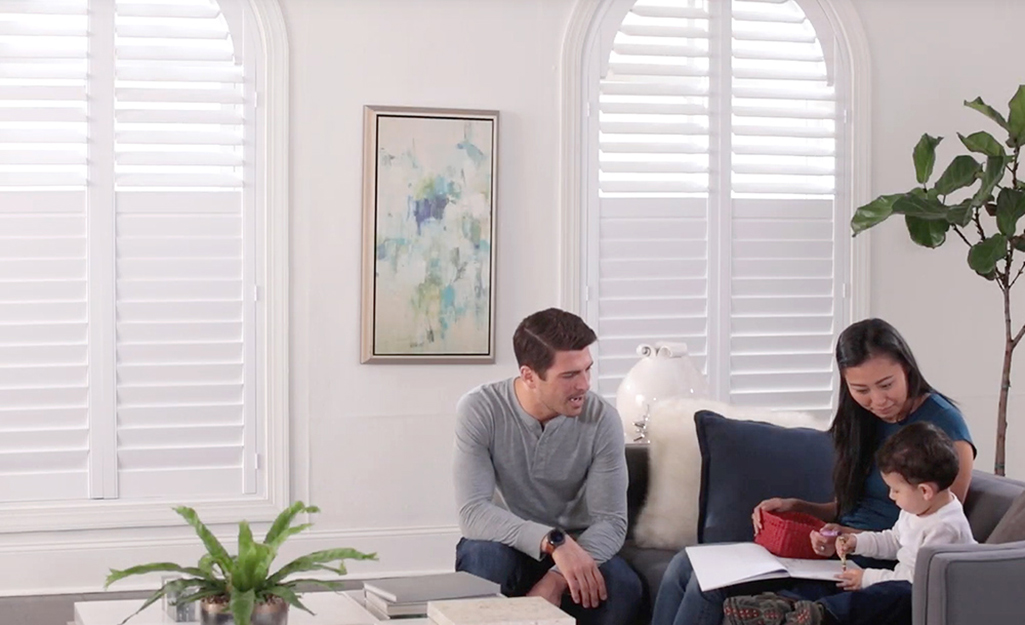 Two parents and a child in a room with window blinds.