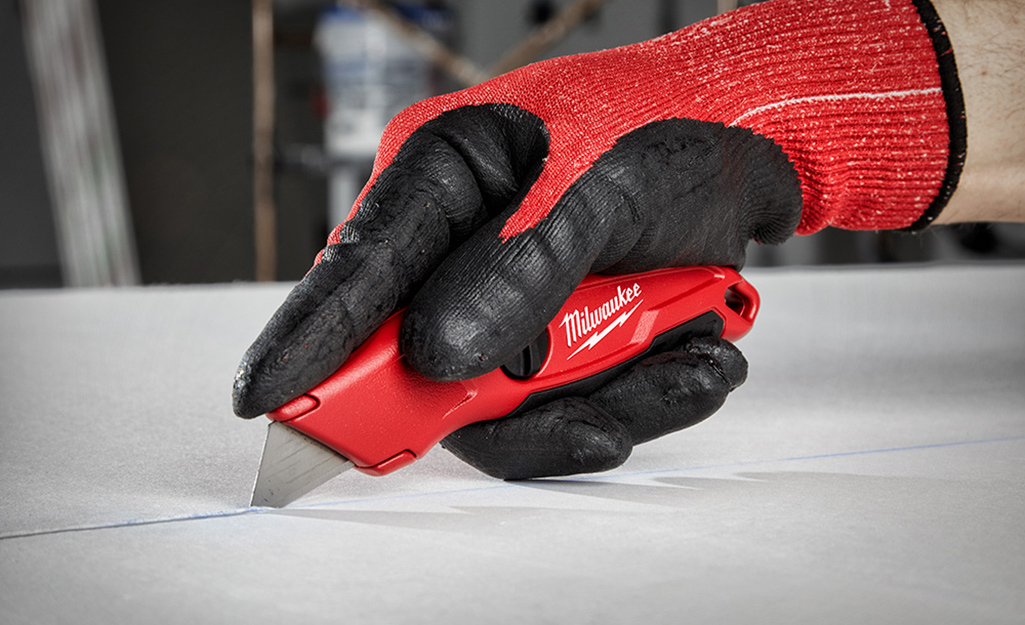 A person wears gloves to use a utility knife.