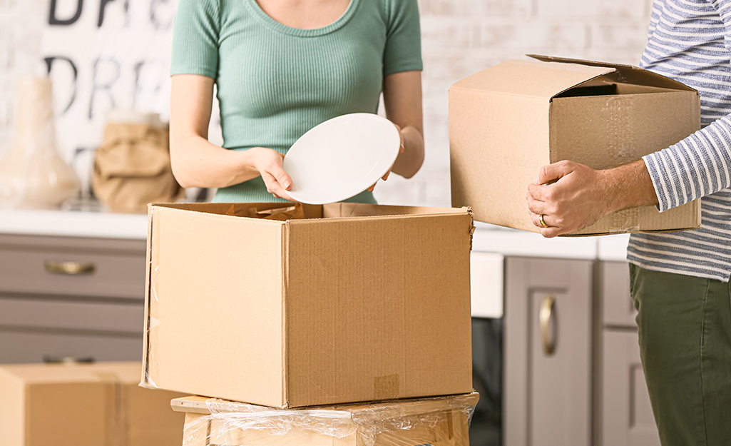 Two women pack dishes into cardboard moving boxes. 