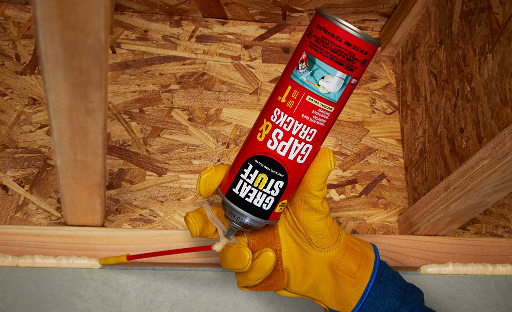 A person uses expandable foam caulk to seal under a wood eave.