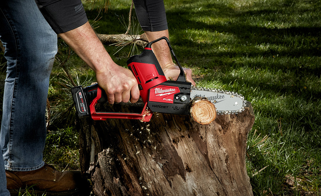 Someone using a small chainsaw to trim a large stump.