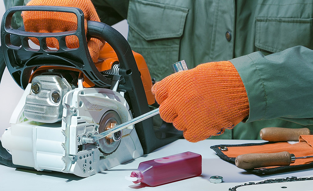 Someone using a wrench to adjust a chainsaw.