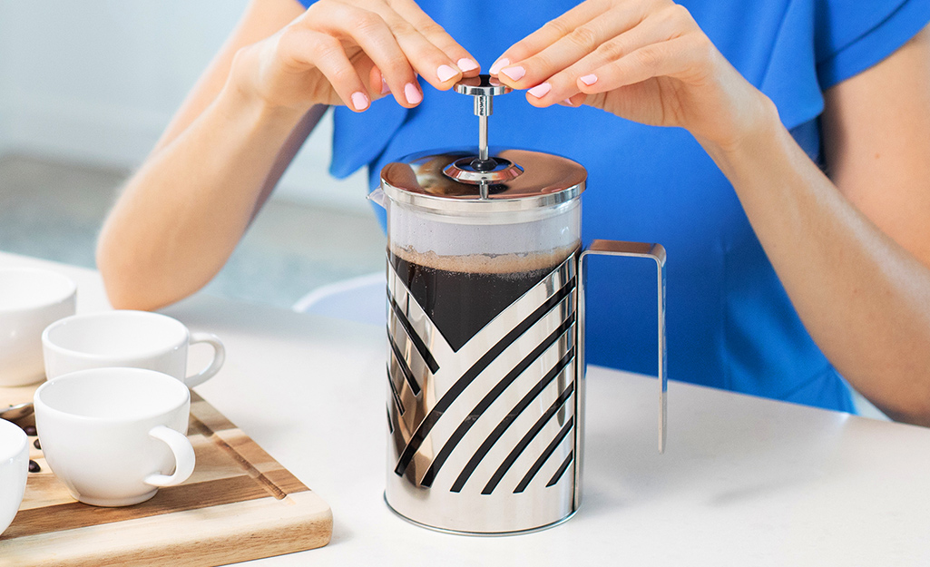 A woman using a French press coffee maker.