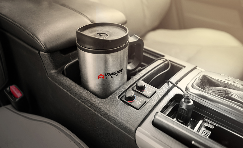 A stainless steel travel mug sits in the cup holder of a car.