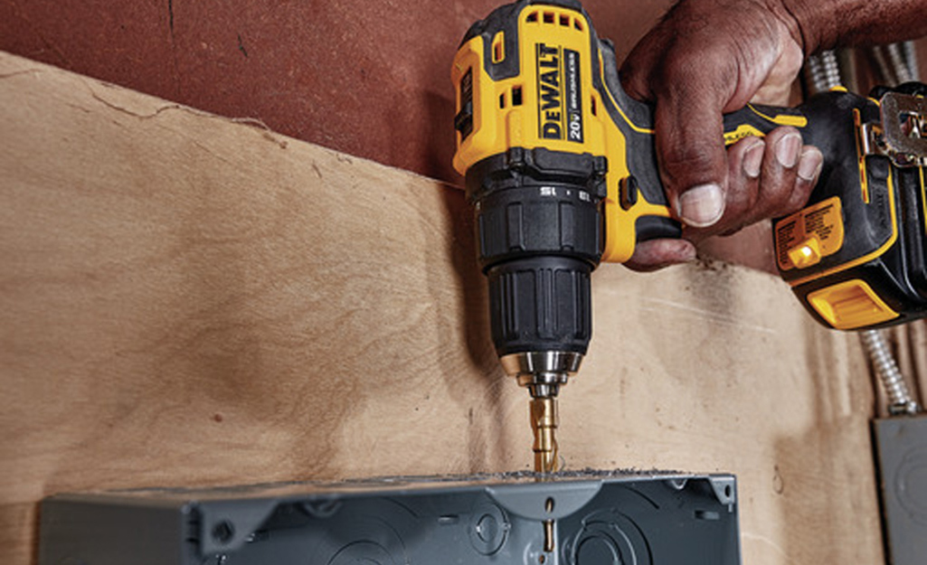 A person uses a cordless drill to attach a box to plywood.