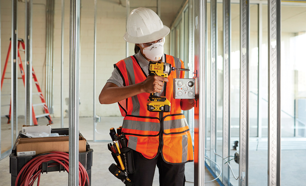 A person wearing safety equipment uses a cordless drill.