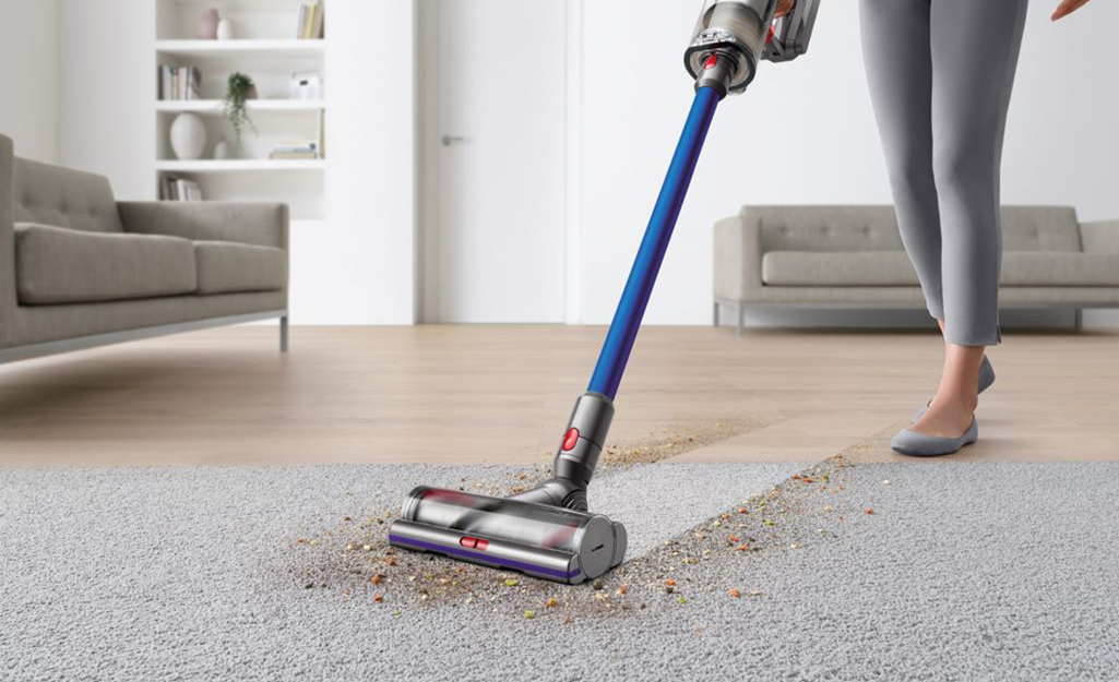 A person uses a cordless vacuum to clean a floor.