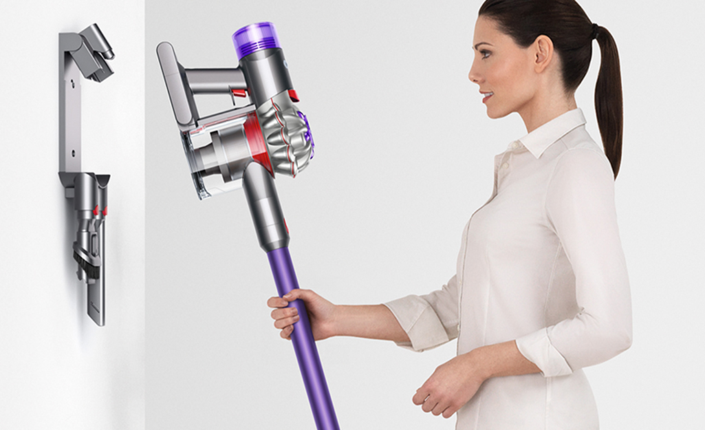A person hangs a cordless vacuum on a wall mount.
