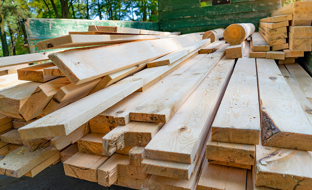 A large stack of deck lumber sits in a backyard.