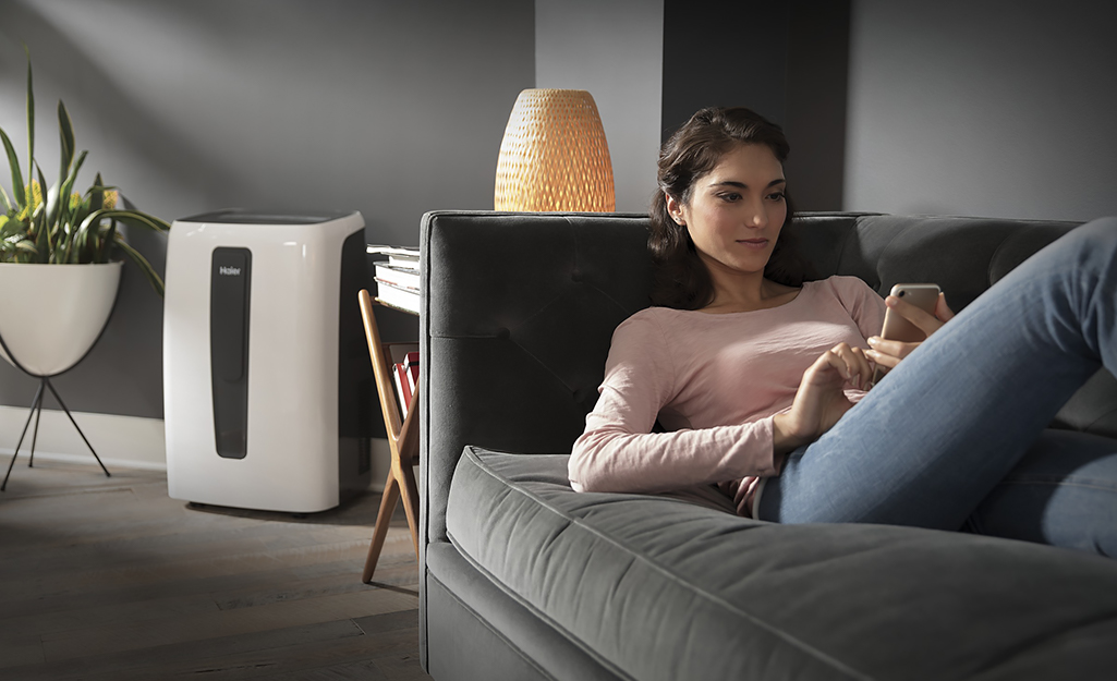 A woman relaxing on her couch while a dehumidifier works in the background.