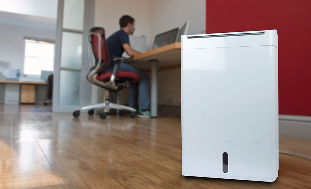 A man works in a home office while using a dehumidifier.