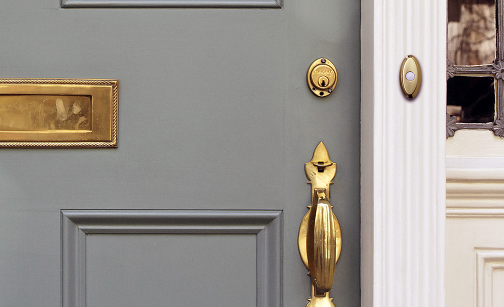 A brass wireless doorbell installed next to a front door with brass hardware.