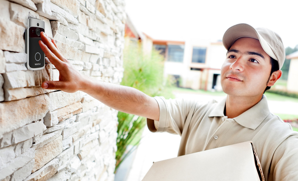 A delivery person ringing a smart doorbell.