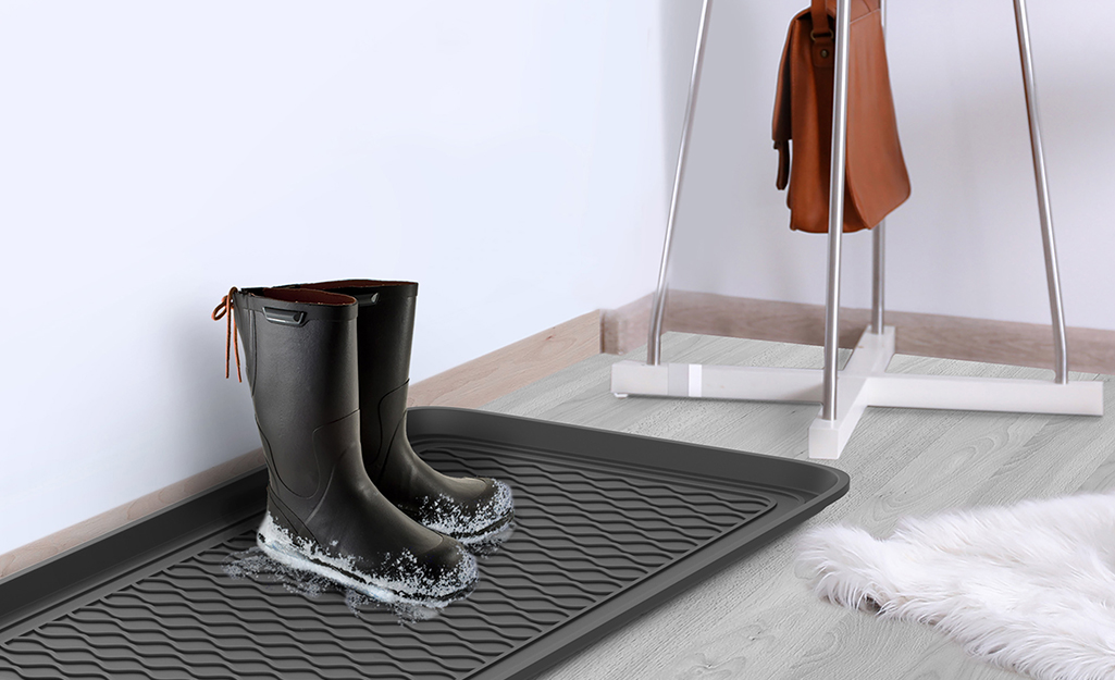A waterproof entryway mat holding a pair of snowy, wet boots.