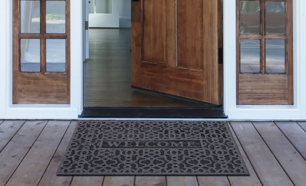 A black rubber doormat lying in front of an open wood door.