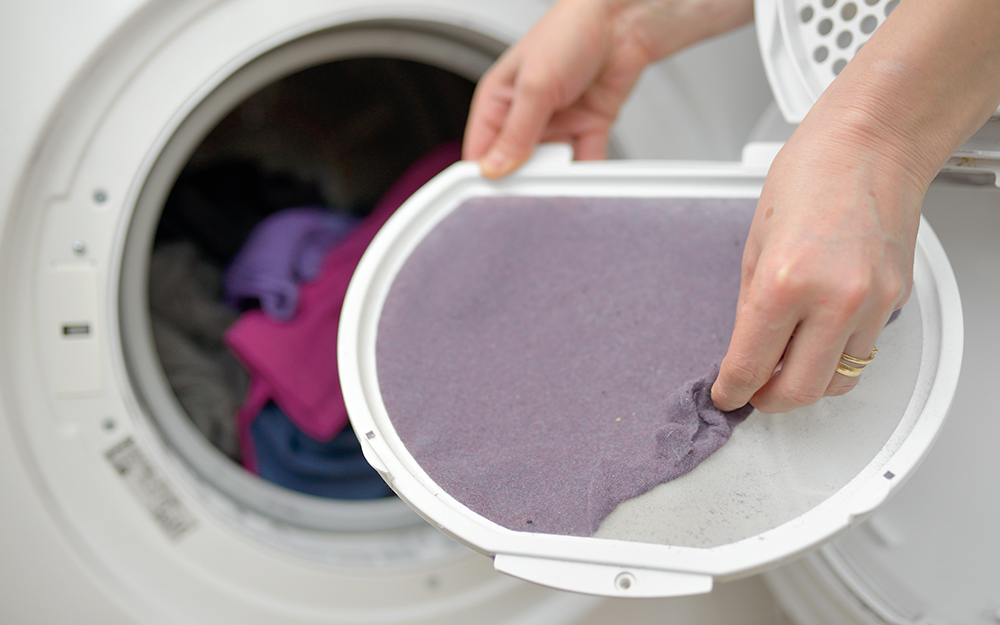 A person removes dryer lint from a dryer filter to clean it. 