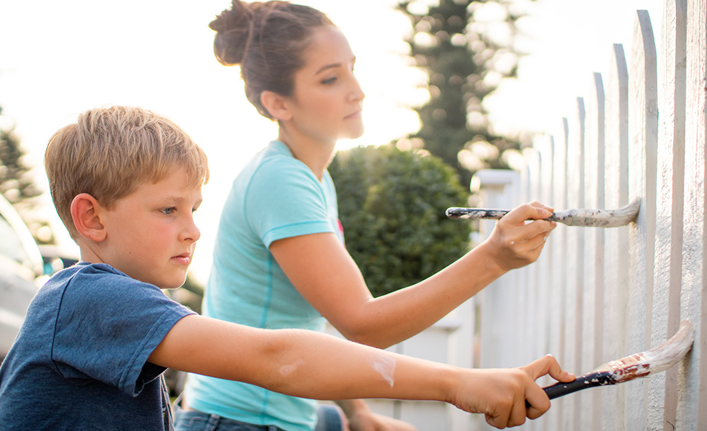 A woman and child painting a fence white.