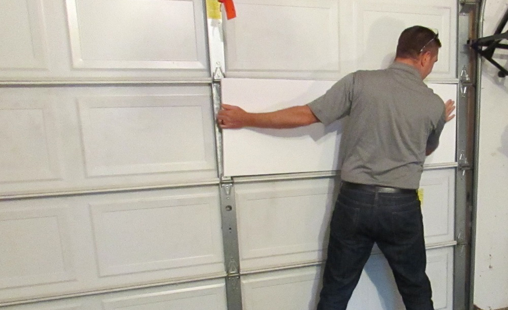 A person installs insulating material to a metal garage door.