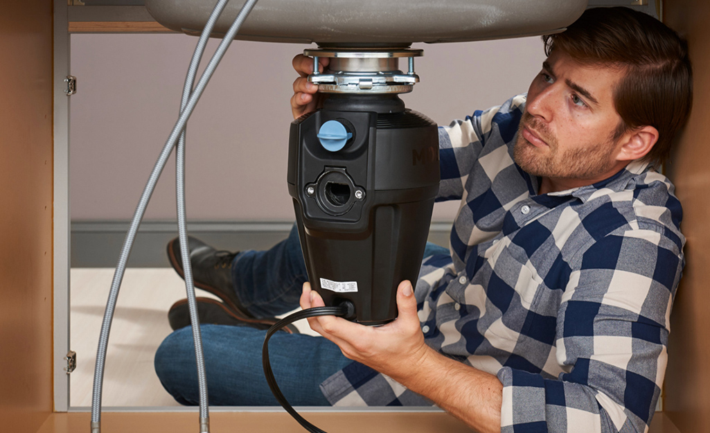 A man installing a garbage disposal underneath a sink.