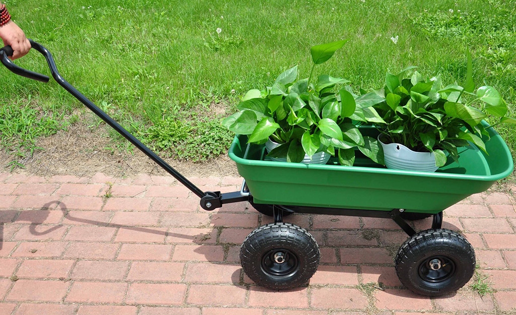 A person pulls a plant-filled garden cart along a brick walkway. 