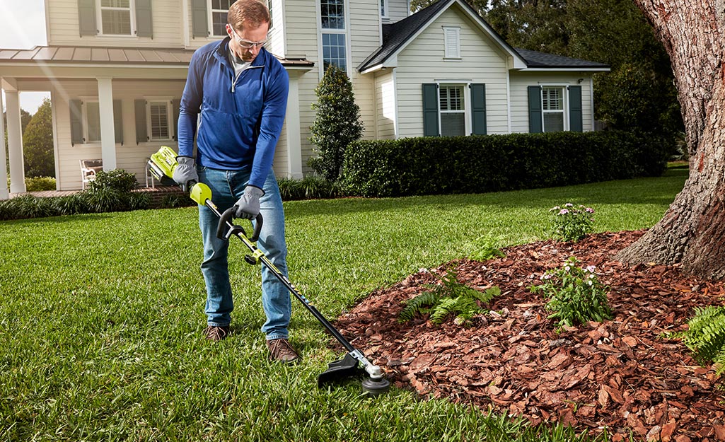 A man uses an edge trimmer to maintain the edge of his lawn.