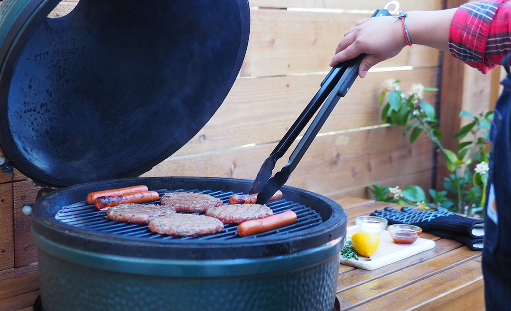 A person uses tongs to flip hot dogs and hamburgers on a grill.