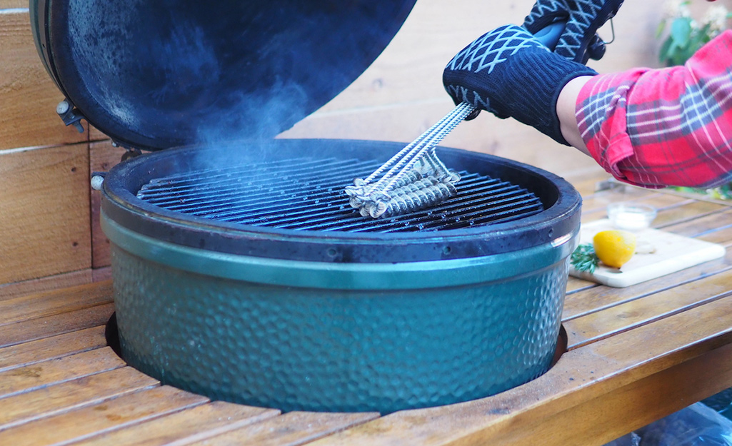 A person uses a grill brush to clean the grate.