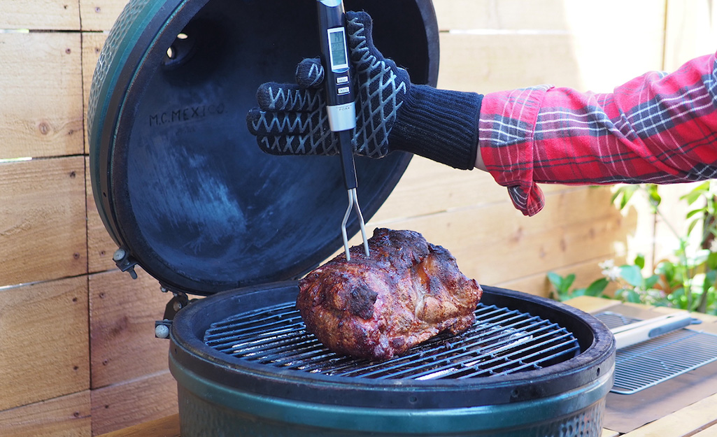 A person uses a digital thermometer to check meat cooking on a grill. 