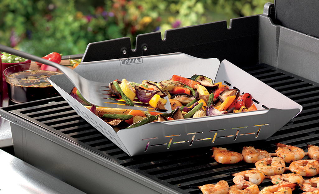 A grilling basket holds vegetables on a grill. 