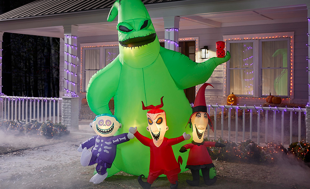 A giant green monster inflatable standing behind three little monsters in front of a house.