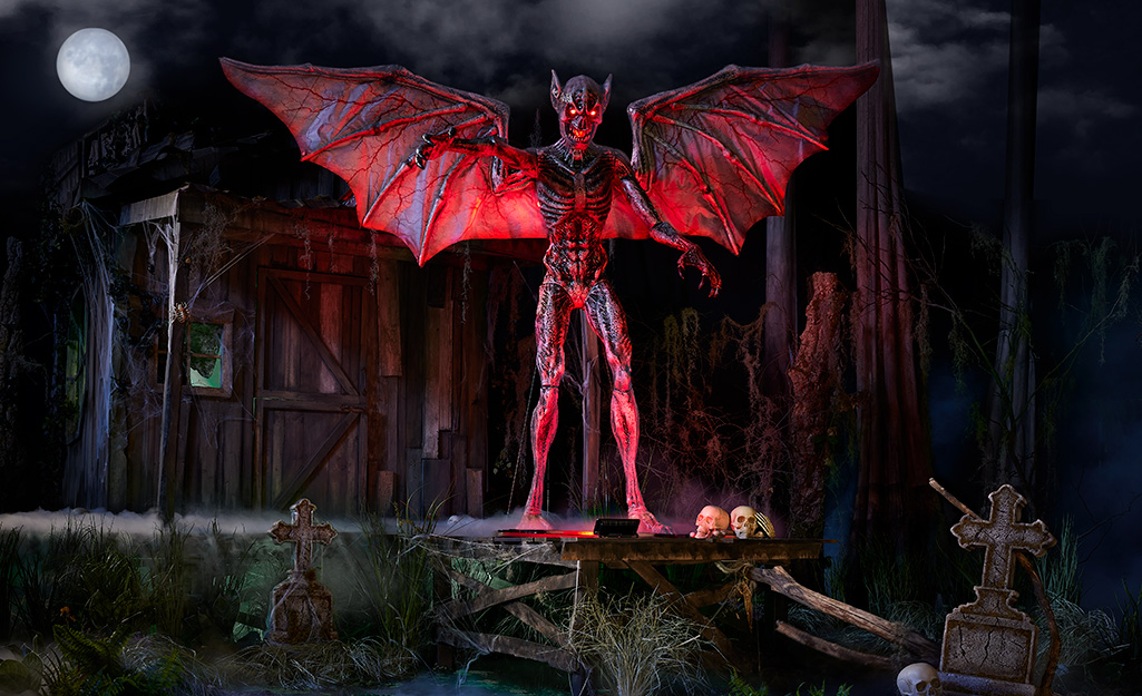 An 8-foot-tall demon extends its lit wings in a dark yard decorated for Halloween.
