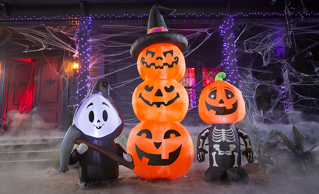 Halloween inflatables such as a stack of jack-'o'-lanterns, a skeleton with a pumpkin head and a smiling Death stand in front of a house.