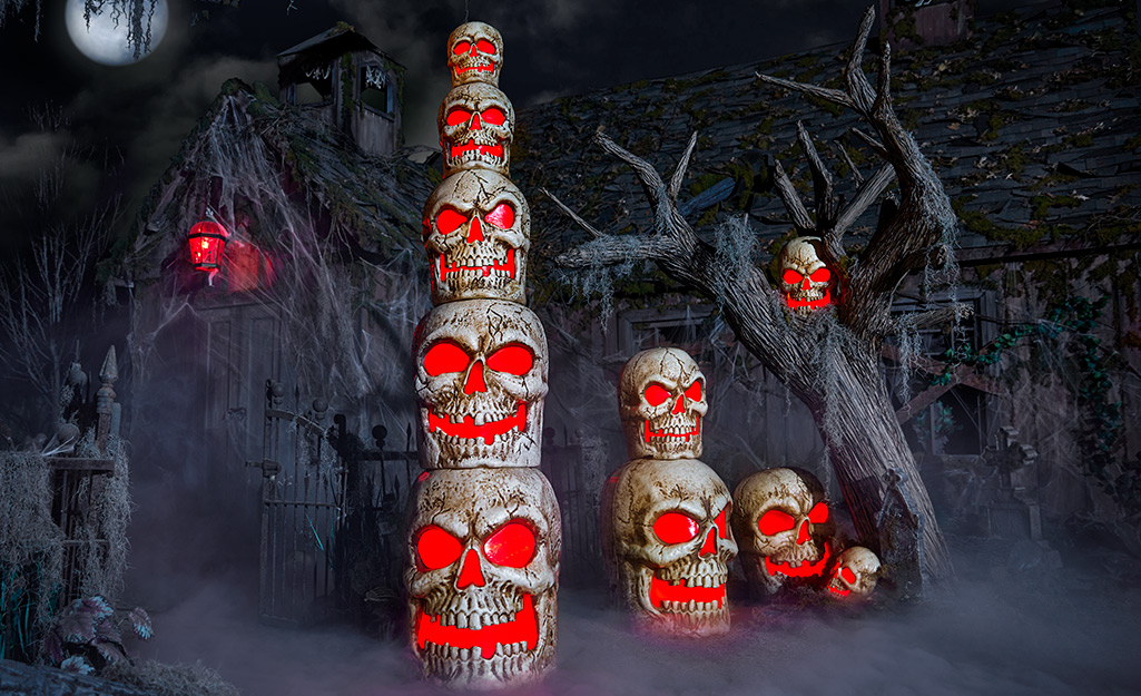 A stack of skulls with glowing red eyes and mouths stand among other skull decor in a spooky scene.