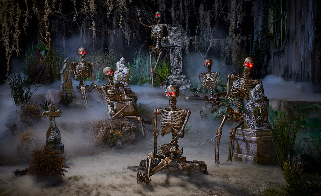 Skeletons with glowing red eyes sit and stand among gravestones in a Halloween cemetery scene.