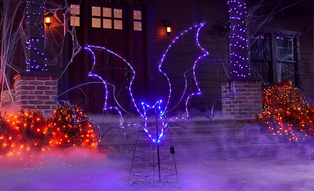 Colorful Halloween light strands and a festive purple bat light up a porch.