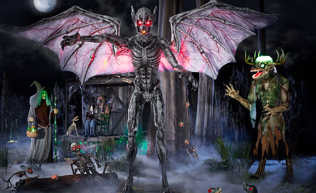 A skeletal demon with glowing eyes and extended wings stands among swamp creatures in a yard decorated for Halloween.