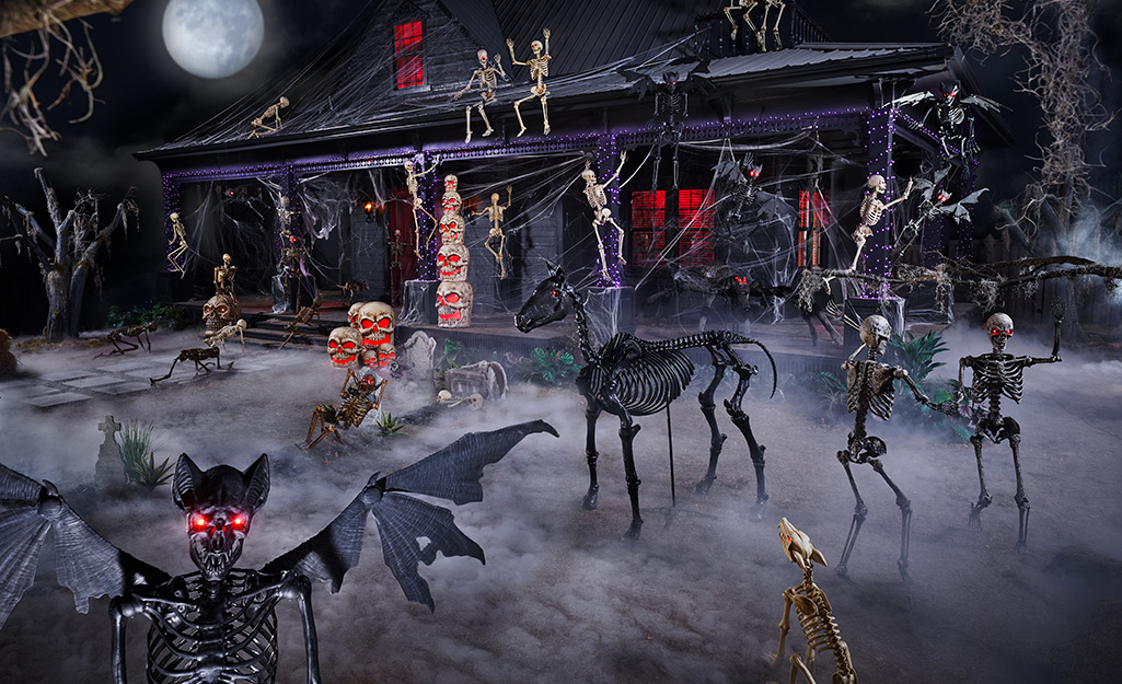 Skeletal creatures stand in a foggy yard in front of a house decorated with skeletons on the roof and porch. 