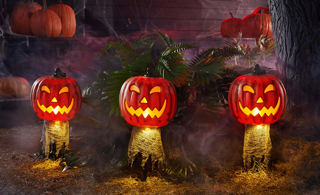Three lit-up Jack-'o'-lanterns stand in a yard decorated for Halloween.