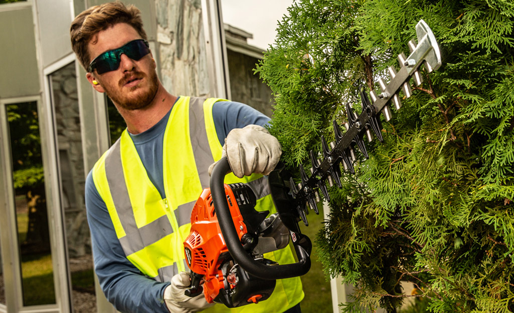 A man wears safety equipment to operate his hedge trimmers.